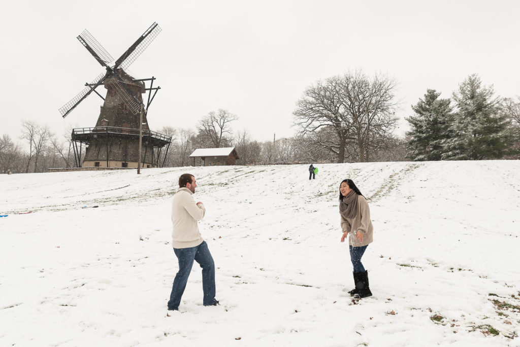 An engagement session for an engaged couple playing snow balls at the windmill at Fabyan Forest Preserve in the winter by a wedding photographer Mila Craila Photography