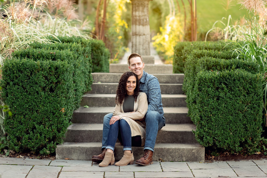 An engagement session for an engaged couple sitting on stairs at Fabyan Forest Preserve in the fall by a wedding photographer Mila Craila Photography