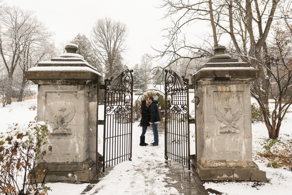 An engagement session for an engaged couple standing behind a metal gate at Fabyan Forest Preserve in the winter by a wedding photographer Mila Craila Photography