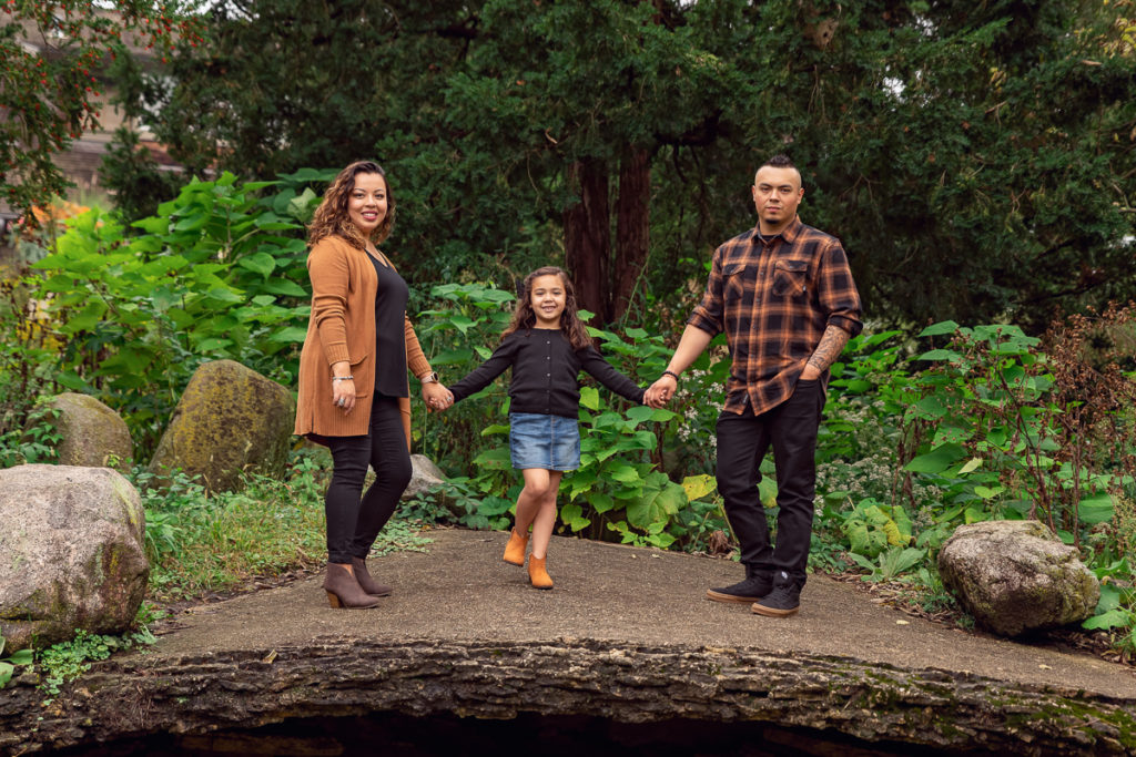 Family session for parents and a young daughter standing on a big stone at Fabyan Forest Preserve in Geneva by family photographer Mila Craila Photography